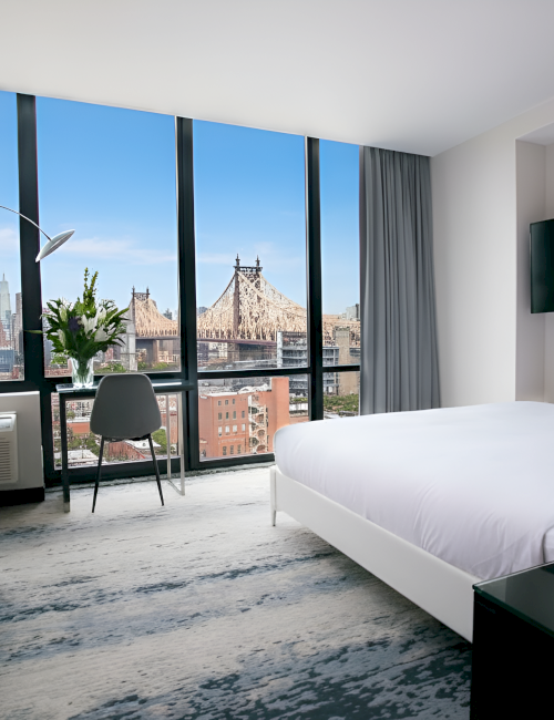 A modern hotel room with large windows, cityscape view, bed, couch, desk, and TV, in a sleek and minimalist design.