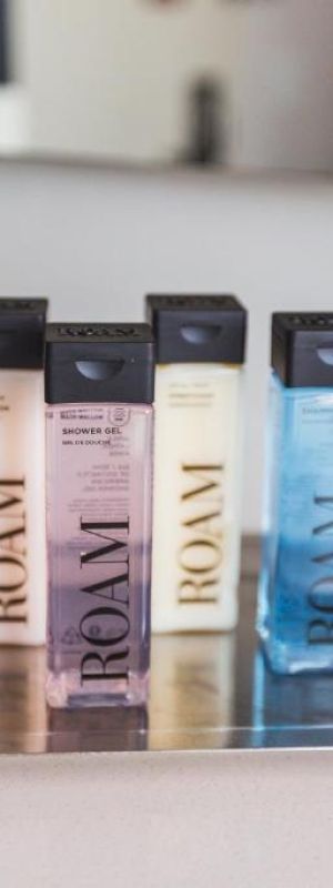 A tray with four Roavi water bottles in pastel colors (pink, gold, blue) and a small white box on a white countertop, blurred background.