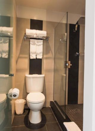 A modern bathroom with a toilet, shower, sink, towels, and a small trash bin.