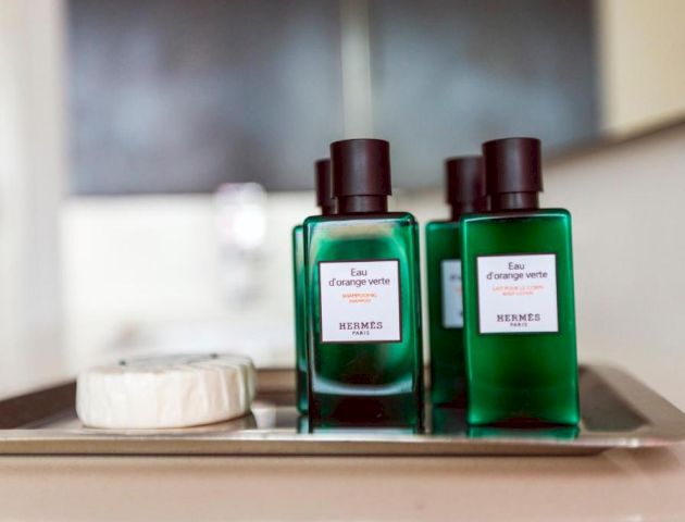 Two green perfume bottles with black caps, a small round container, all on a metal tray.