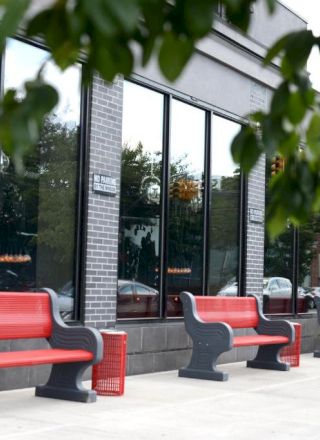 A row of red and gray benches outside a modern glass-front building, with trees and reflections in the windows.